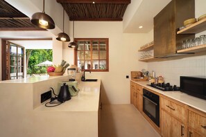 Une cuisine moderne avec des meubles en bois, un four encastré et un plan de travail sur lequel se trouvent une bouilloire et un mixeur.