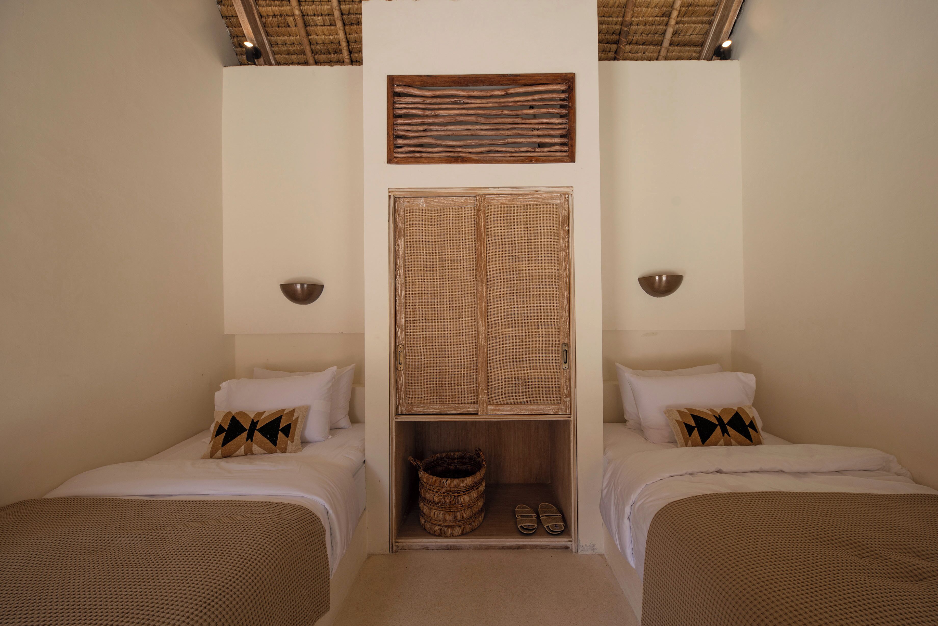 A bedroom with two beds, a wardrobe, and a woven basket.