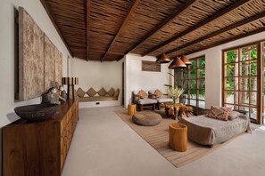 Een ruime woonkamer met een hoge plafond, een zithoek, een houten salontafel en een groot raam met uitzicht op groen.