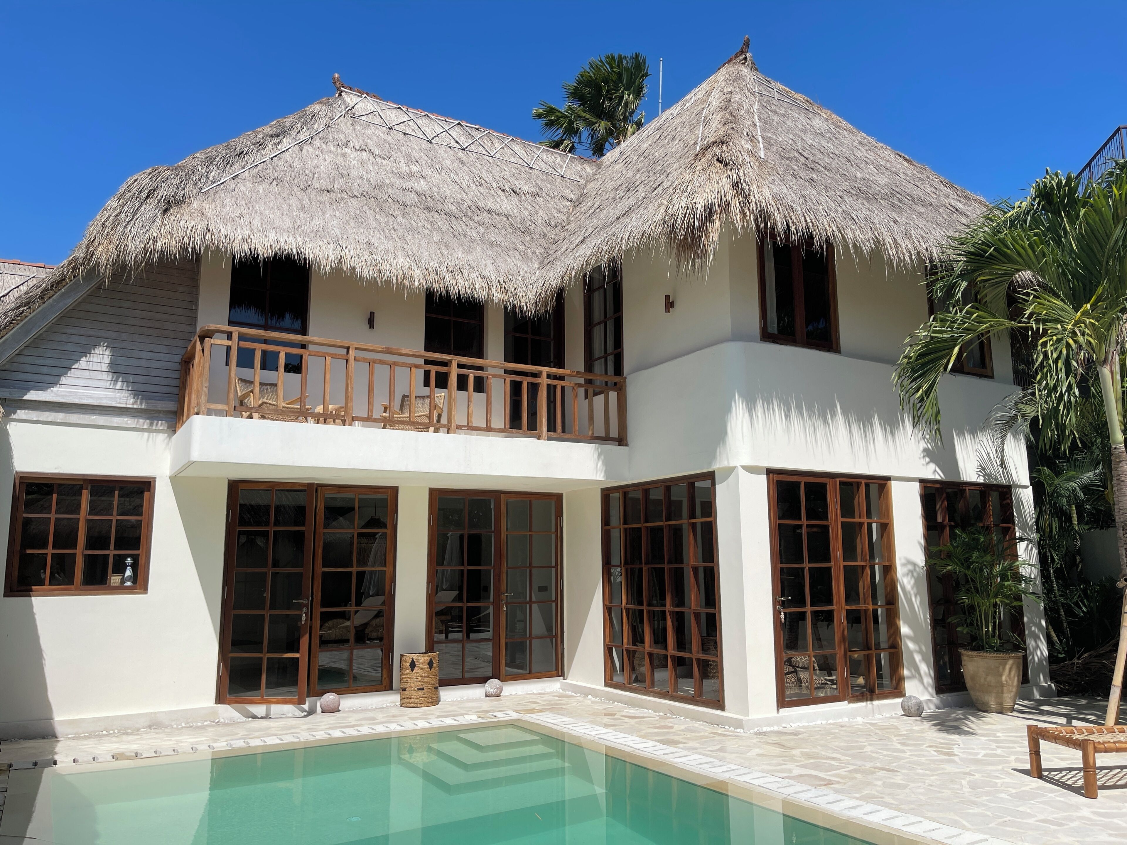 A two-story building with a pool, large windows, and a thatched roof.