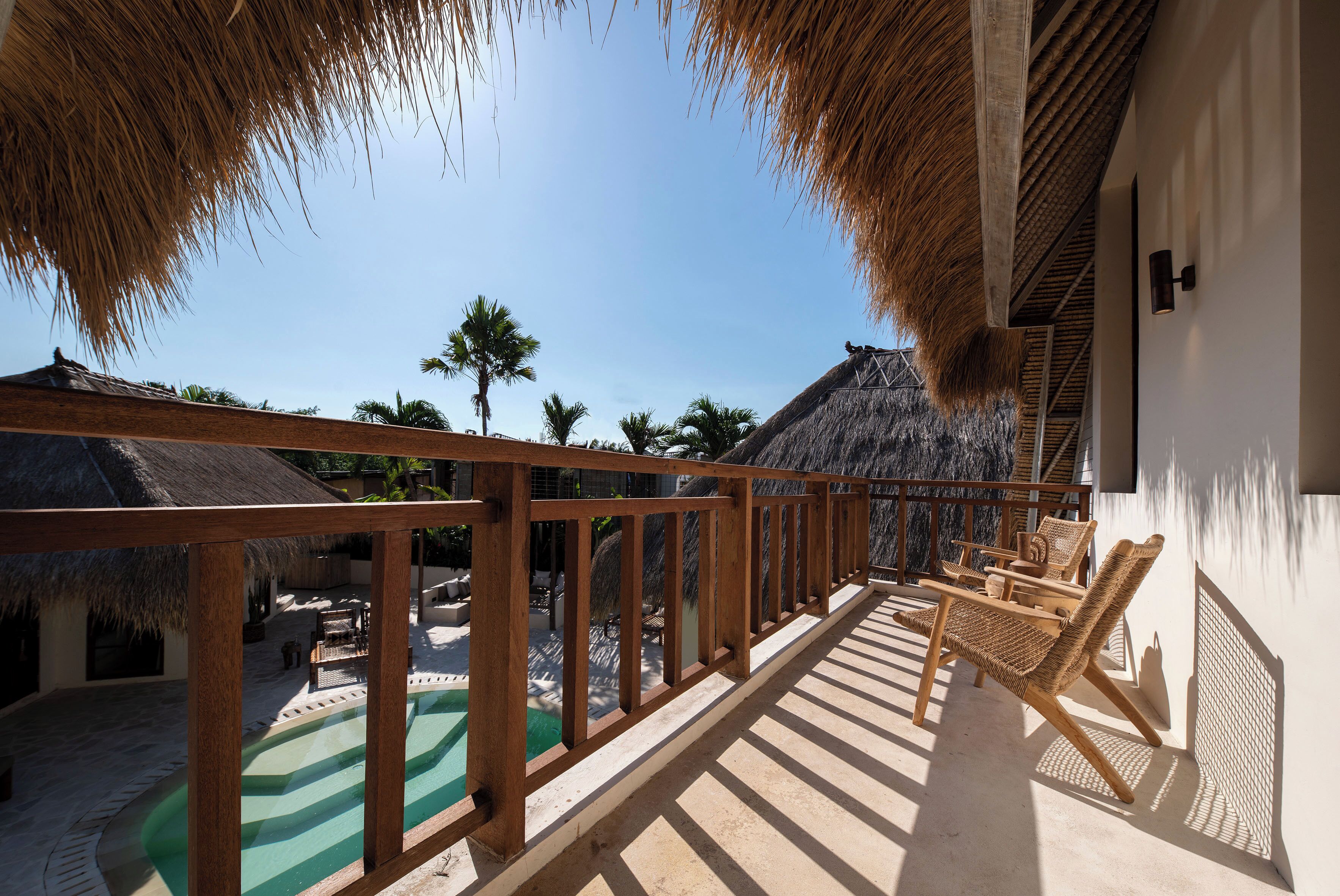 A wooden balcony with a view of a pool and palm trees.