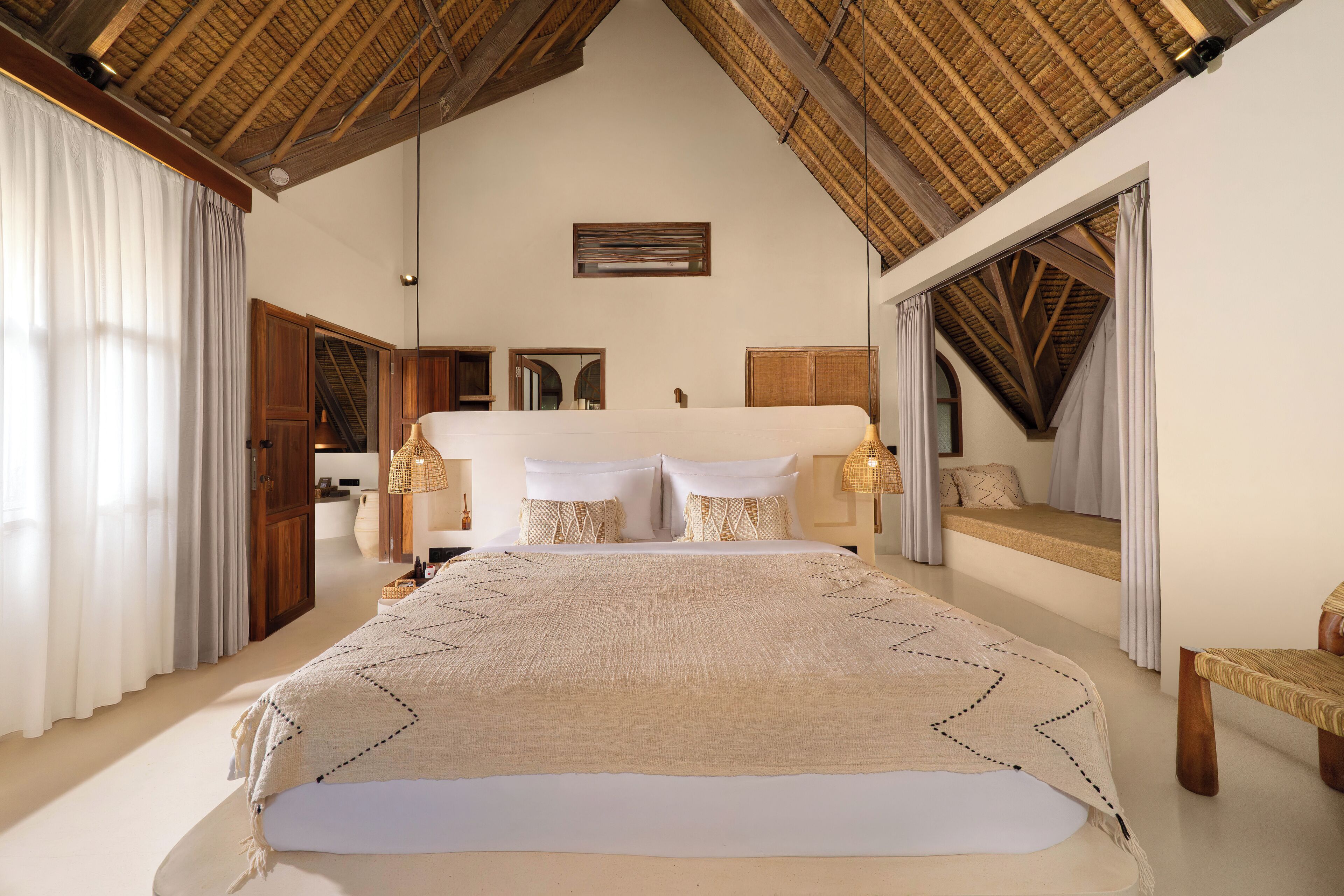 Een ruime slaapkamer met een groot bed, houten balken in het plafond en uitzicht op een balkon.
