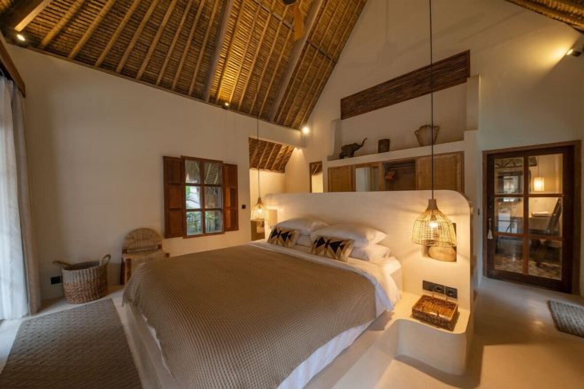 A spacious bedroom with a large bed, a wooden ceiling, and a built-in shelf with decorative items.