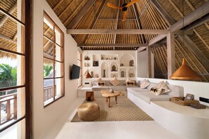 A room with a thatched roof, a sofa set, a television, and decorative items on the walls. - Villa Xanadu Pererenan by Nakula (Canggu)