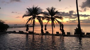 Une vue sur le coucher de soleil, avec des palmiers et un espace de détente au bord de la piscine.