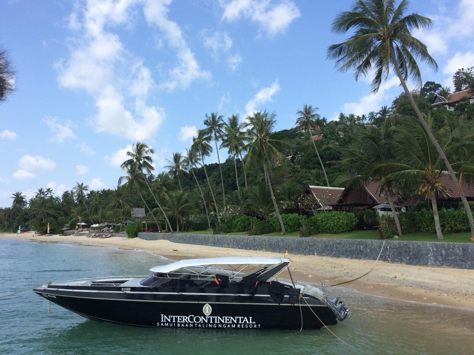 Un motoscafo nero ormeggiato su una spiaggia, con un resort sullo sfondo.