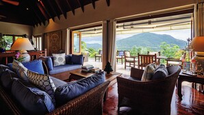 Un vaste espace de vie comprenant un canapé, des fauteuils et une table, et offrant de grandes fenêtres avec vue sur les montagnes.