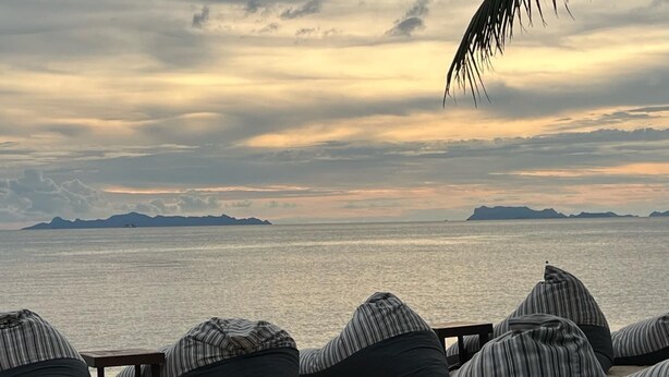 Des fauteuils en forme de sac de haricots sur une plage, avec vue sur la mer et les montagnes au loin.