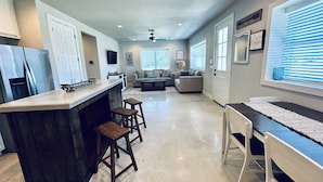 A modern kitchen with a bar area, a dining table, and a living room with a sofa and a coffee table. - Near Chandelier of Gruene, Downtown & Whitewater – Game Room, Fire Pit & More! (New Braunfels)