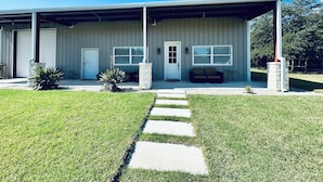 A modern building with a covered porch, a front door, and a small seating area. - Near Chandelier of Gruene, Downtown & Whitewater – Game Room, Fire Pit & More! (New Braunfels)