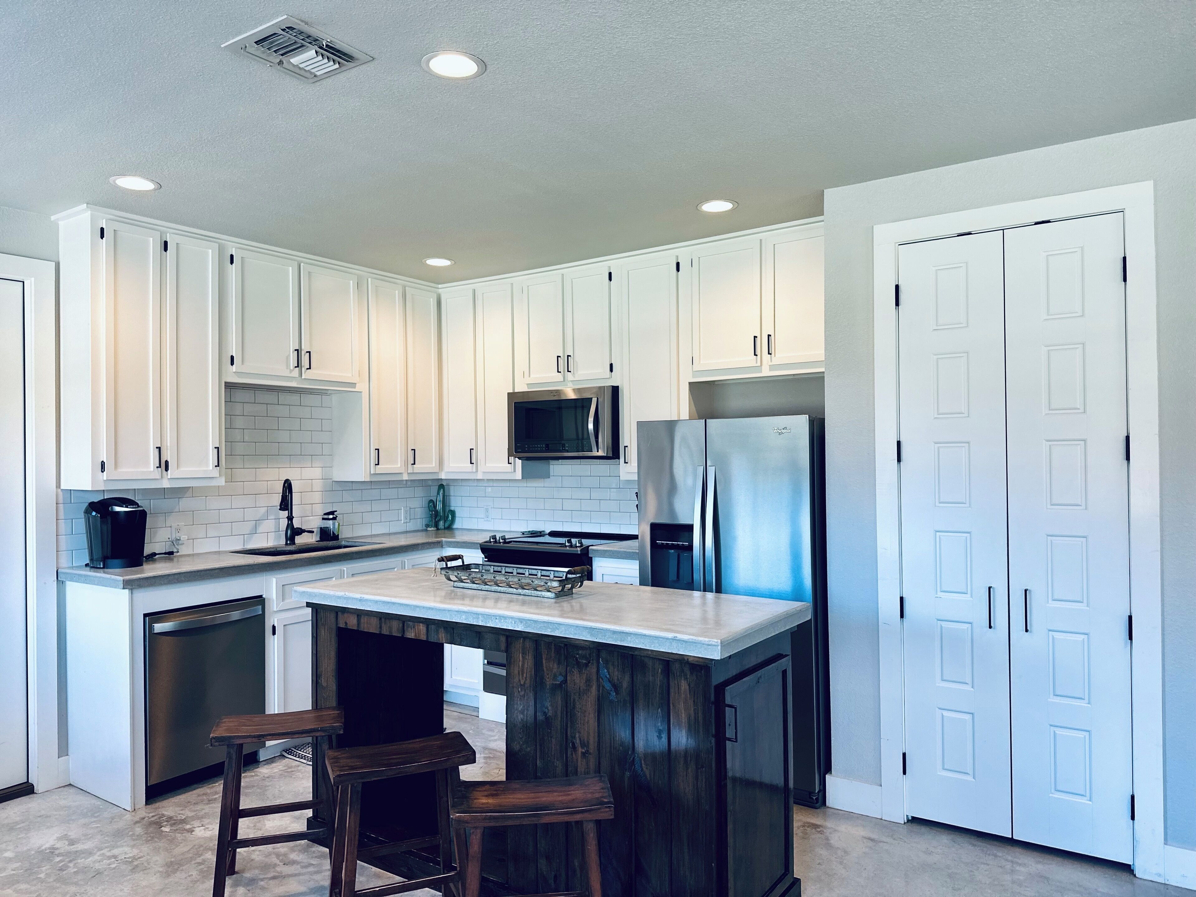 Una cocina moderna con armarios blancos, electrodomésticos de acero inoxidable y una isla central con taburetes.