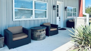 A covered outdoor seating area with two wicker sofas and a stone fire pit. - Near Chandelier of Gruene, Downtown & Whitewater – Game Room, Fire Pit & More! (New Braunfels)