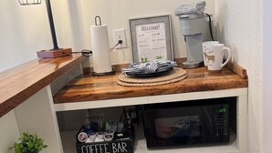 Una kitchenette con una máquina de café, un letrero que dice "COFFEE BAR" y un microondas en un estante.