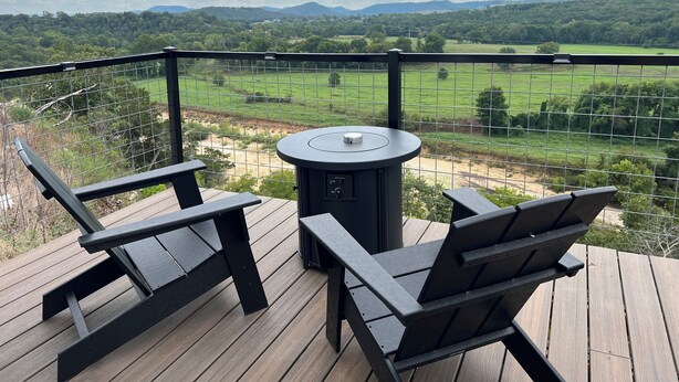 Una terraza con dos sillas y una mesa, con vista a un campo cercado y colinas distantes.