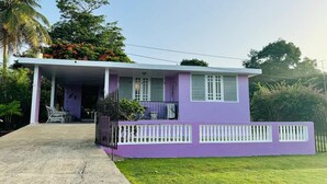 Einbungalow mit violetten Wänden, einer überdachten Veranda und einem weißen Zaun.