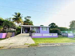 Un petit bâtiment d’un seul étage, à la façade violette et au porche blanc.