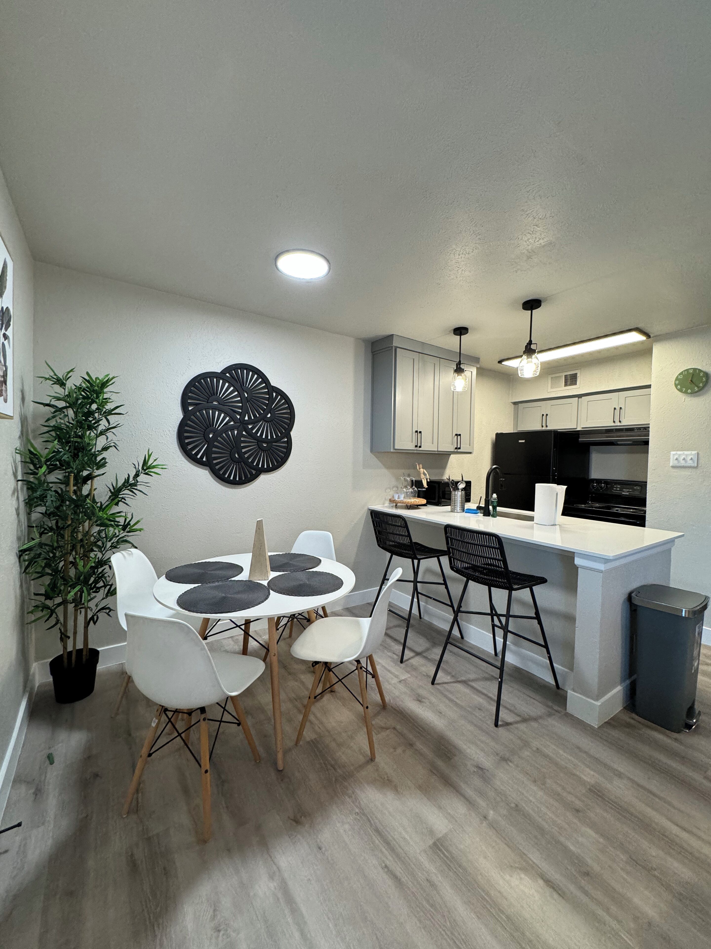 A modern kitchen with white cabinets, a black refrigerator, and a dining area with a round table and chairs.