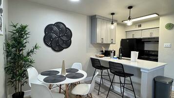 A modern kitchen with white cabinets, a black refrigerator, and a dining area with a round table and chairs.