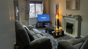 Un salon comprenant un ensemble de canapés, un téléviseur, une cheminée et une fenêtre avec des rideaux.