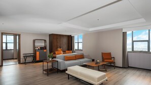 A modern living room with a sofa, a coffee table, and a bench. There is a kitchen area with a counter and cabinets. The room has large windows and a view of the city. - UrCove by Hyatt Suzhou Shantang Street (Suzhou)