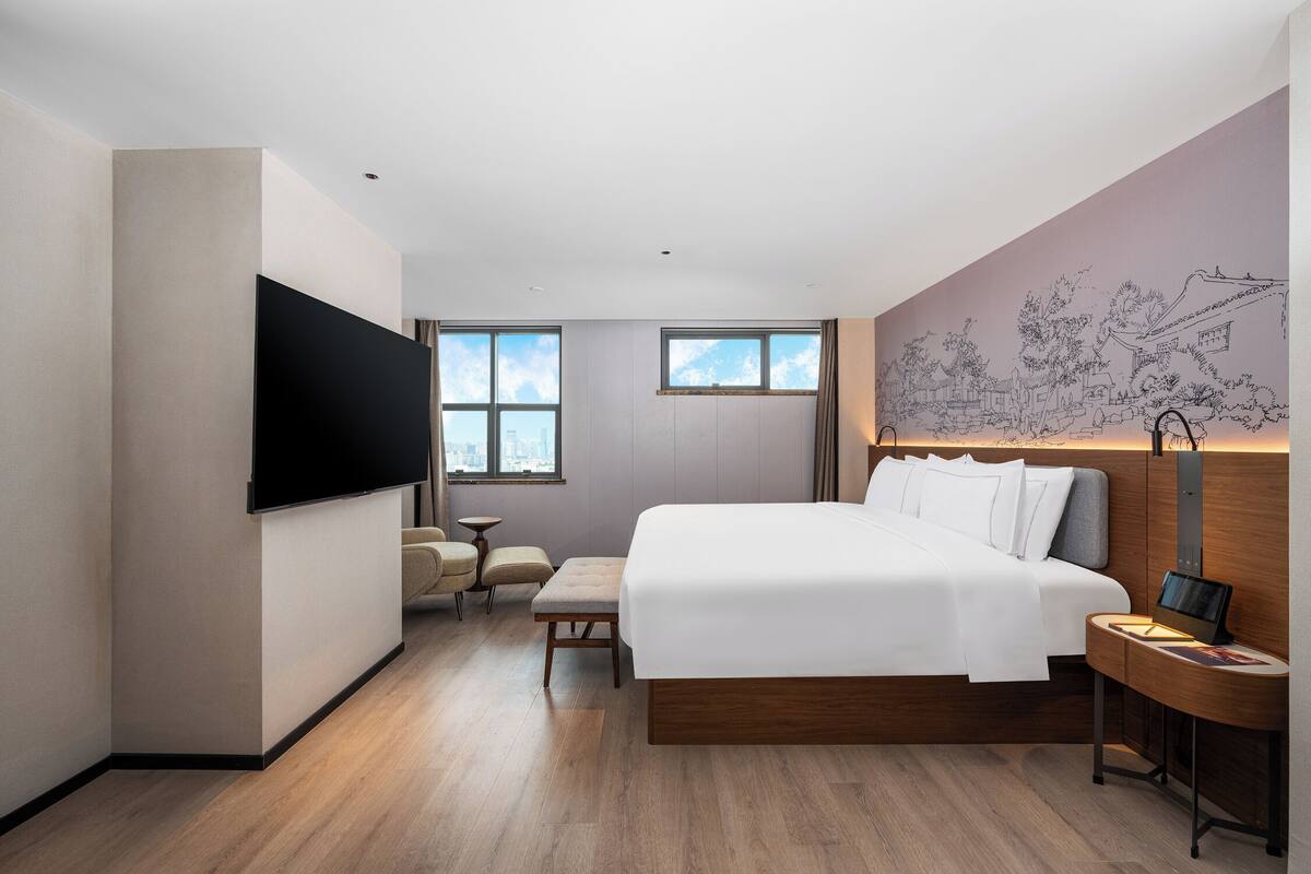 A modern hotel room with a large bed, a flat-screen TV, a bedside table, and a wall mural.