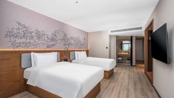 Habitación de hotel con dos camas, un mural grande en la pared y un televisor montado.