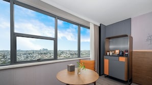 A modern hotel room with a large window offering a city view, a round table with a vase of flowers, and a small kitchenette. - UrCove by Hyatt Suzhou Shantang Street (Suzhou)