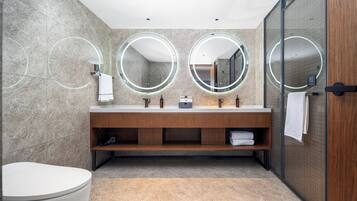 A modern bathroom with a marble wall, a wooden vanity, a toilet, and a glass shower enclosure.
