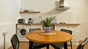 A compact kitchen with a washing machine, microwave, and a small dining area with a round wooden table and four chairs. - MarketHome Ecolodge Plataneras (Lomo Del Balo (Guia I.))