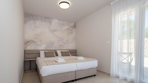 A modern bedroom with a large bed, a headboard with abstract art, a bedside table, and a view through sheer curtains to the outdoors. - Holiday House Jewel With Private Pool (Krk)