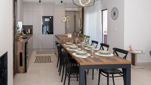 A modern dining area with a wooden table set for six, black chairs, and a kitchen in the background. - Holiday House Jewel With Private Pool (Krk)