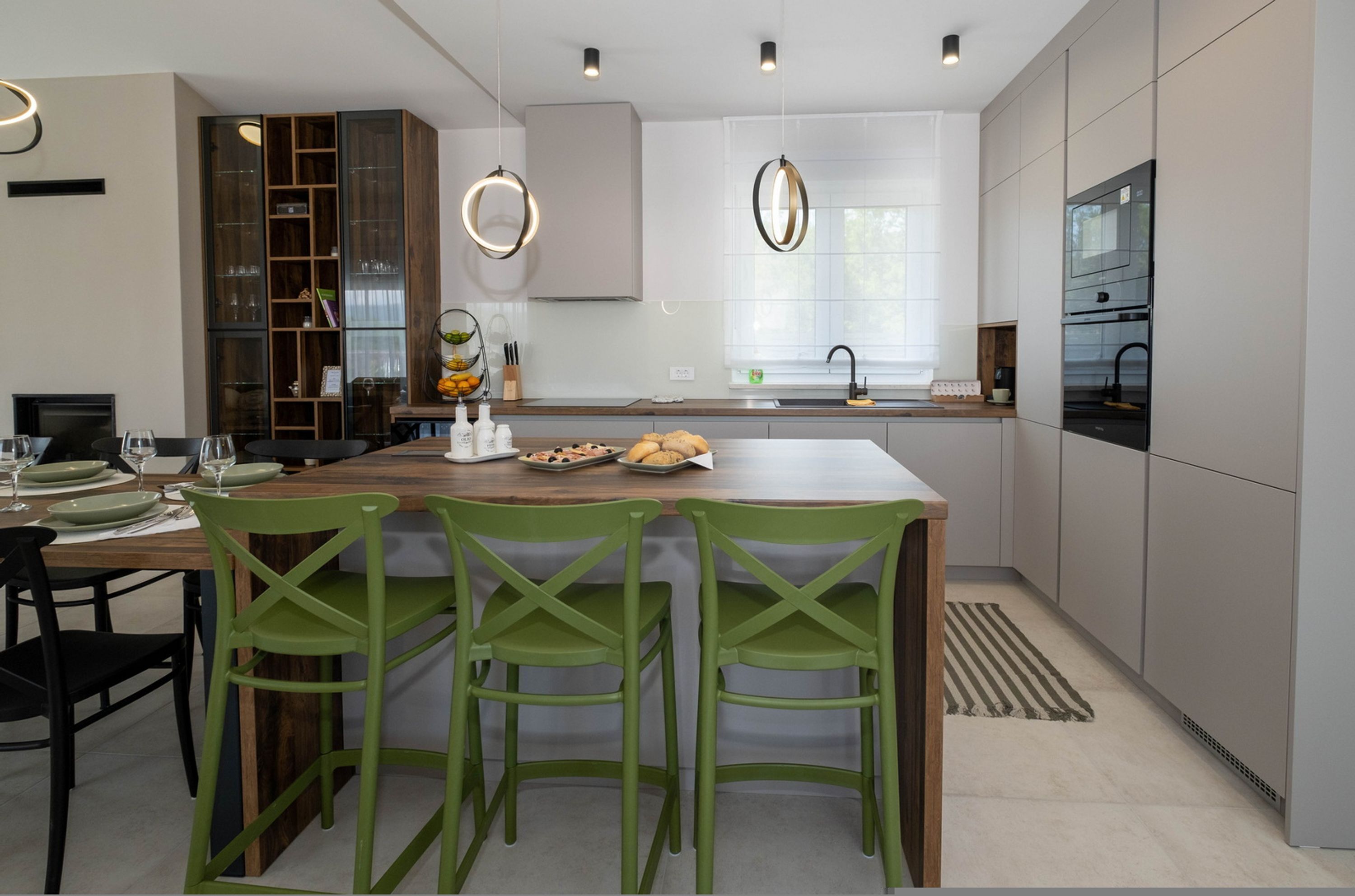 Una cocina moderna con una isla central, sillas verdes y una estantería empotrada para vinos.