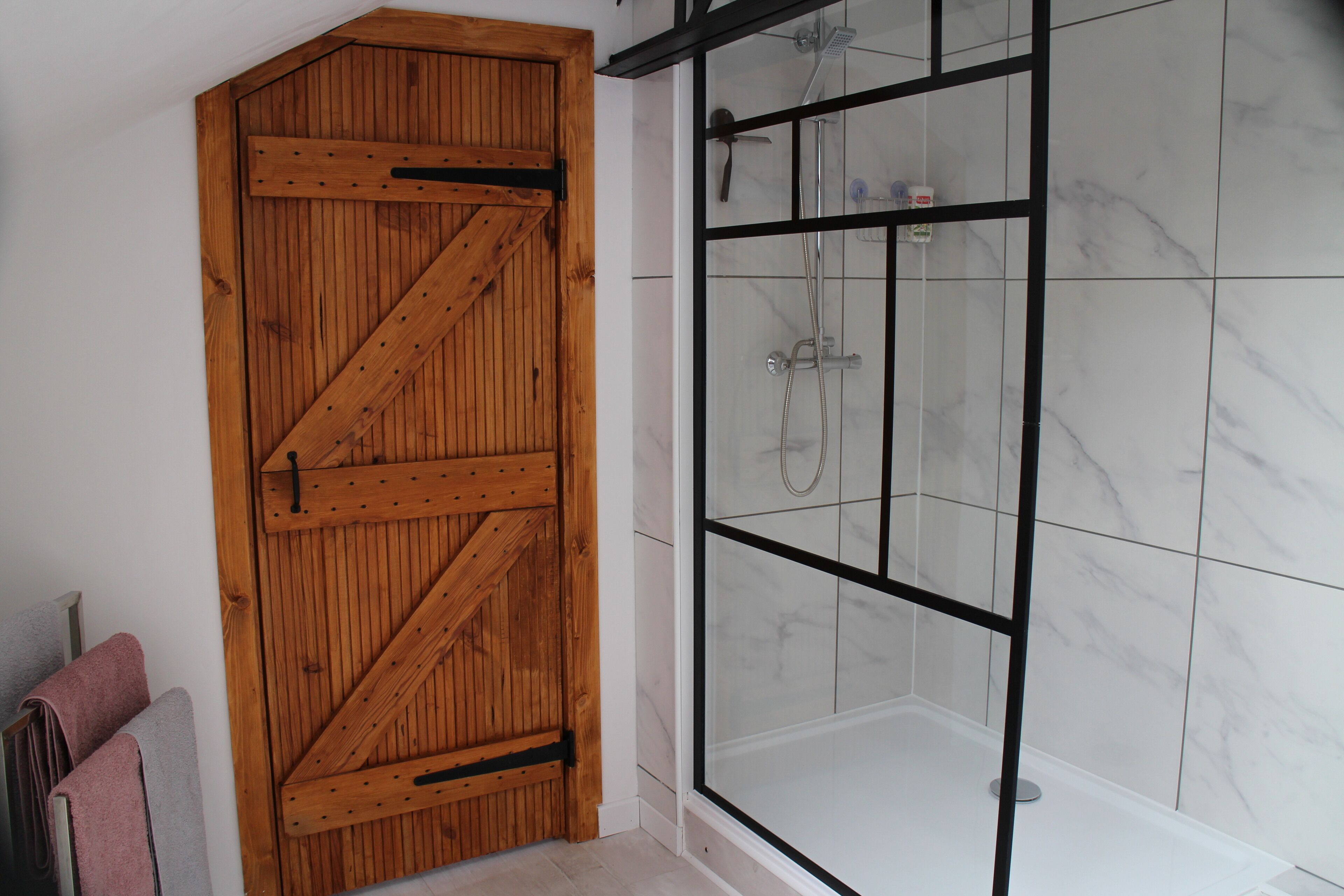 A wooden door with a diagonal brace design, a glass shower enclosure with a black frame, and a tiled floor.