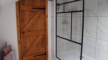 A wooden door with a diagonal brace design, a glass shower enclosure with a black frame, and a tiled floor.