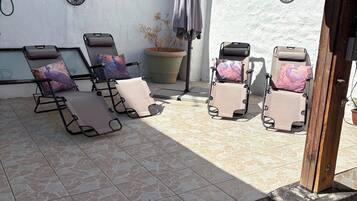 A patio with four sun loungers, a potted plant, and decorative wall art.
