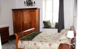 A bedroom with a wooden bed, a dresser, a window with a view, and a chandelier.