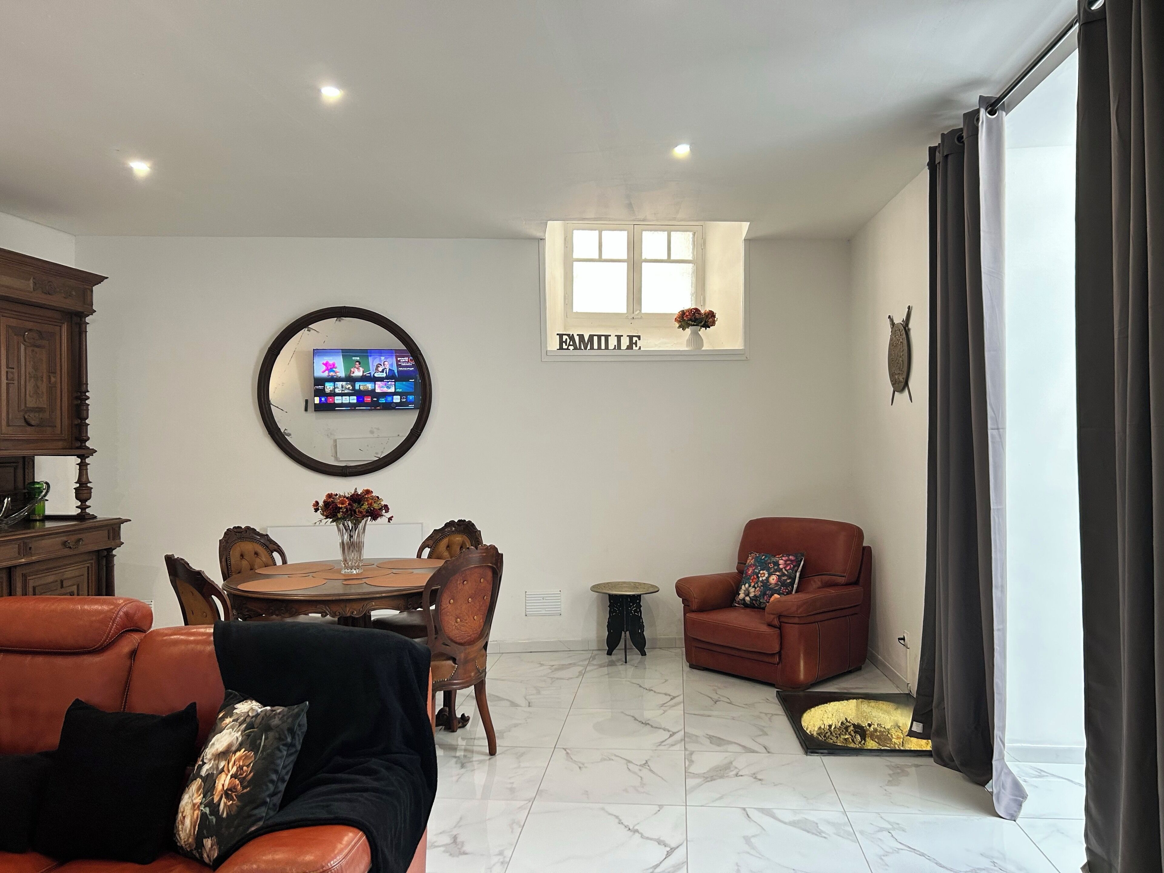 A living room with a TV, a dining table, a sofa, a chair, and a fireplace.