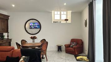 A living room with a TV, a dining table, a sofa, a chair, and a fireplace.
