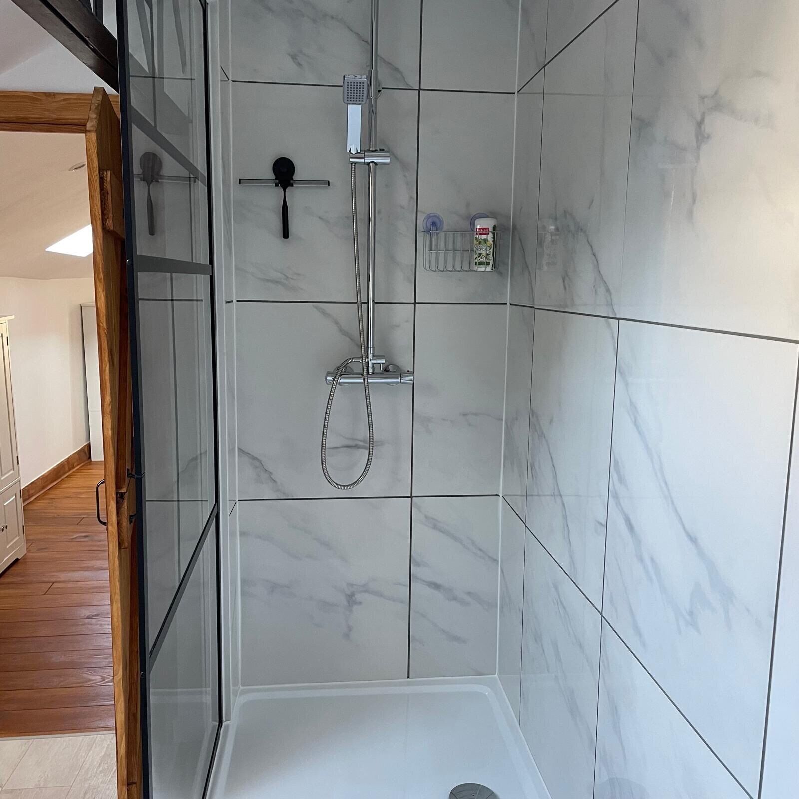 Un baño moderno con cabina de ducha de vidrio, azulejos de mármol y un cabezal de ducha manual.