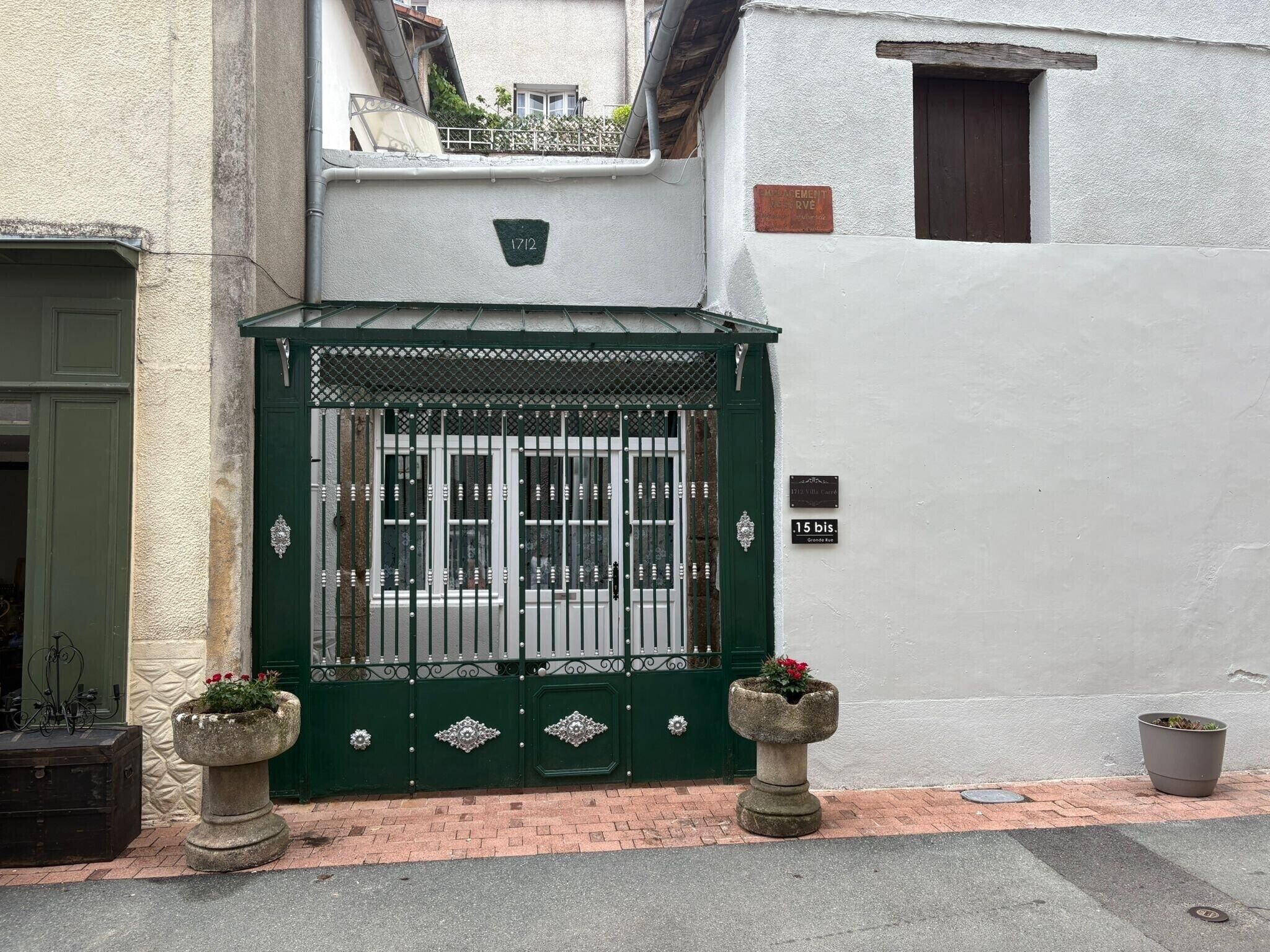 A gated entrance with a green gate, a potted plant on the left, and a potted plant on the right.
