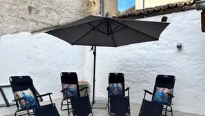 A patio with four black folding chairs, each with a peacock-themed cushion, under a large black umbrella.