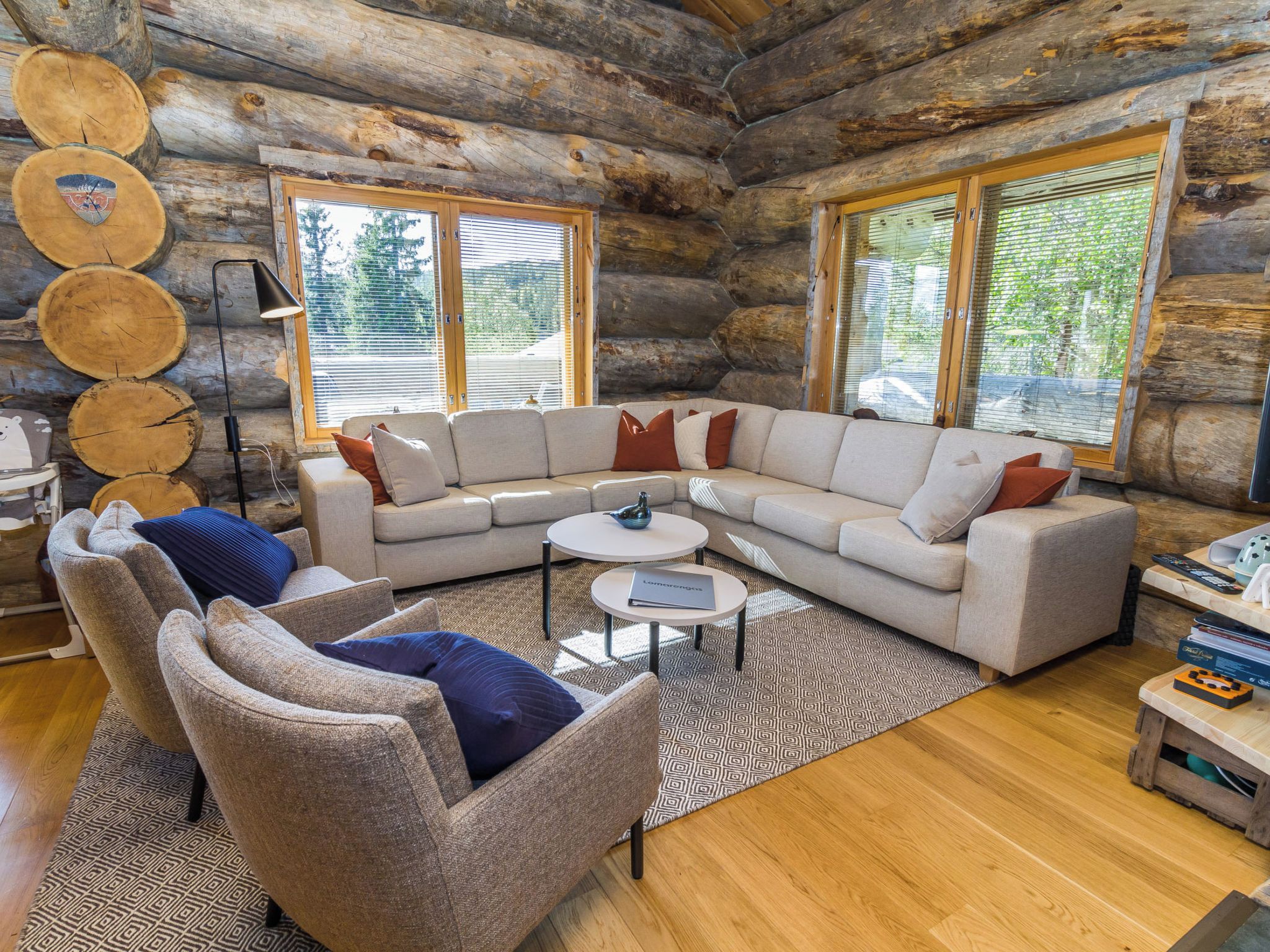 L’intérieur d’une cabane en rondins, avec un canapé d’angle, des fauteuils, une table basse et une cheminée.