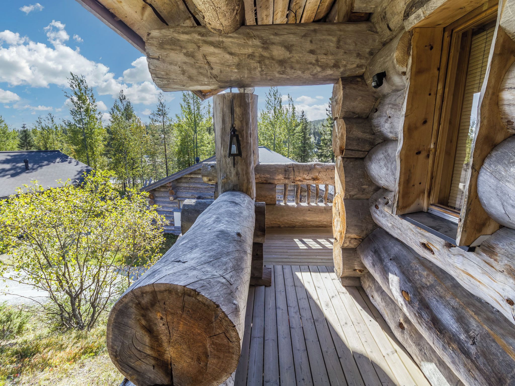 Une cabane en rondins avec une terrasse en bois, un grand tronc d’arbre au premier plan et une vue sur la forêt environnante.