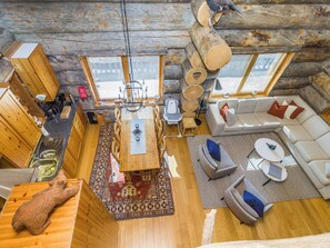 A cozy cabin interior with a dining area, sofa, and a large wooden log structure.