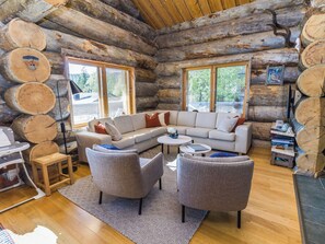 Interior d'una cabana de fusta amb un sofà modular, dues butaques, una taula de centre i una zona de menjador.