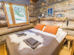 A log cabin bedroom with a bed, pillows, a fur rug, and a window with blinds.