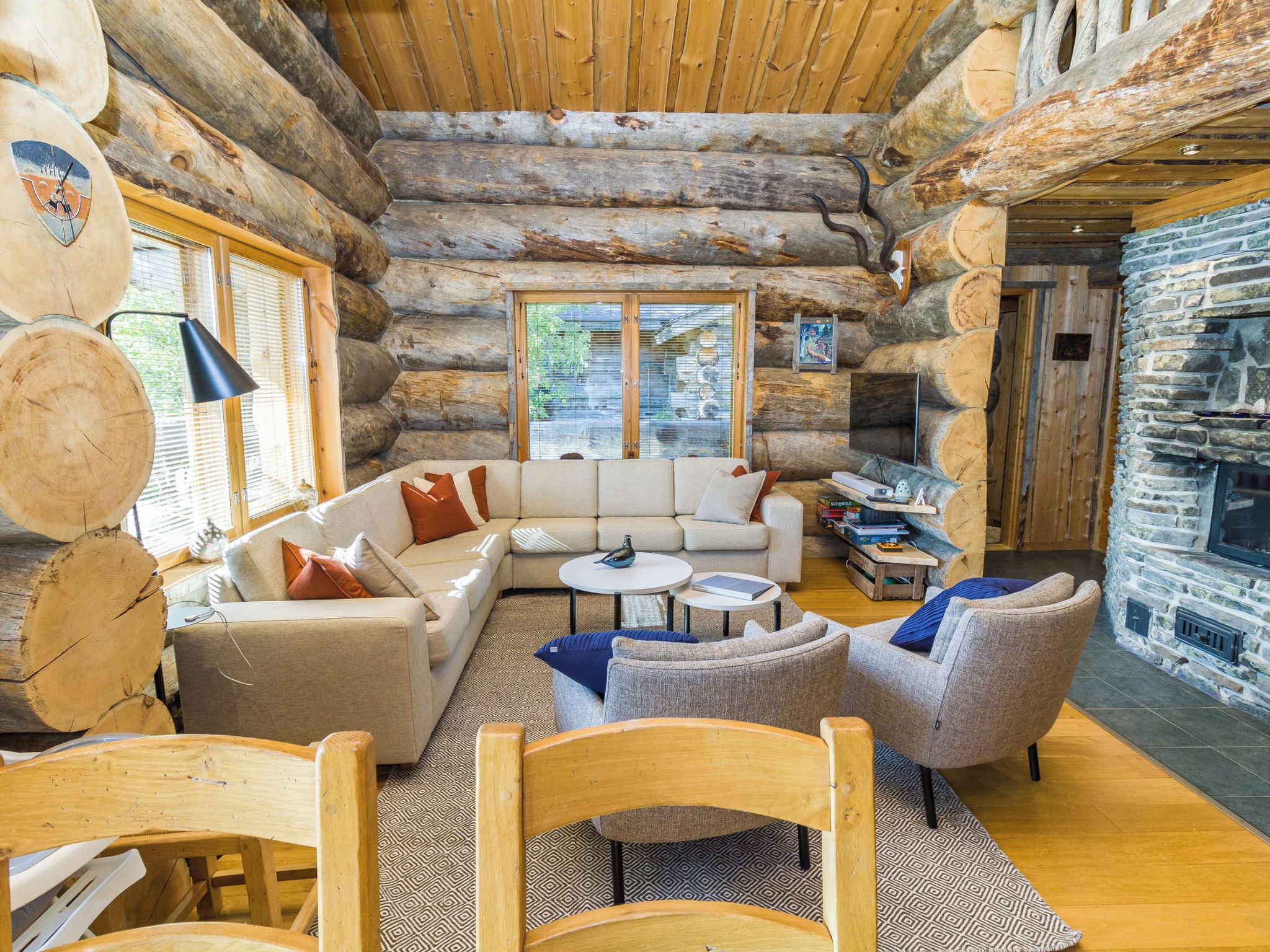 L’intérieur d’une cabane en rondins, avec un canapé, des fauteuils, une cheminée et un mur en pierre.