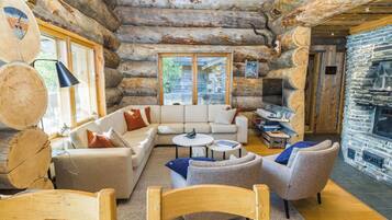L’intérieur d’une cabane en rondins, avec un canapé, des fauteuils, une cheminée et un mur en pierre.