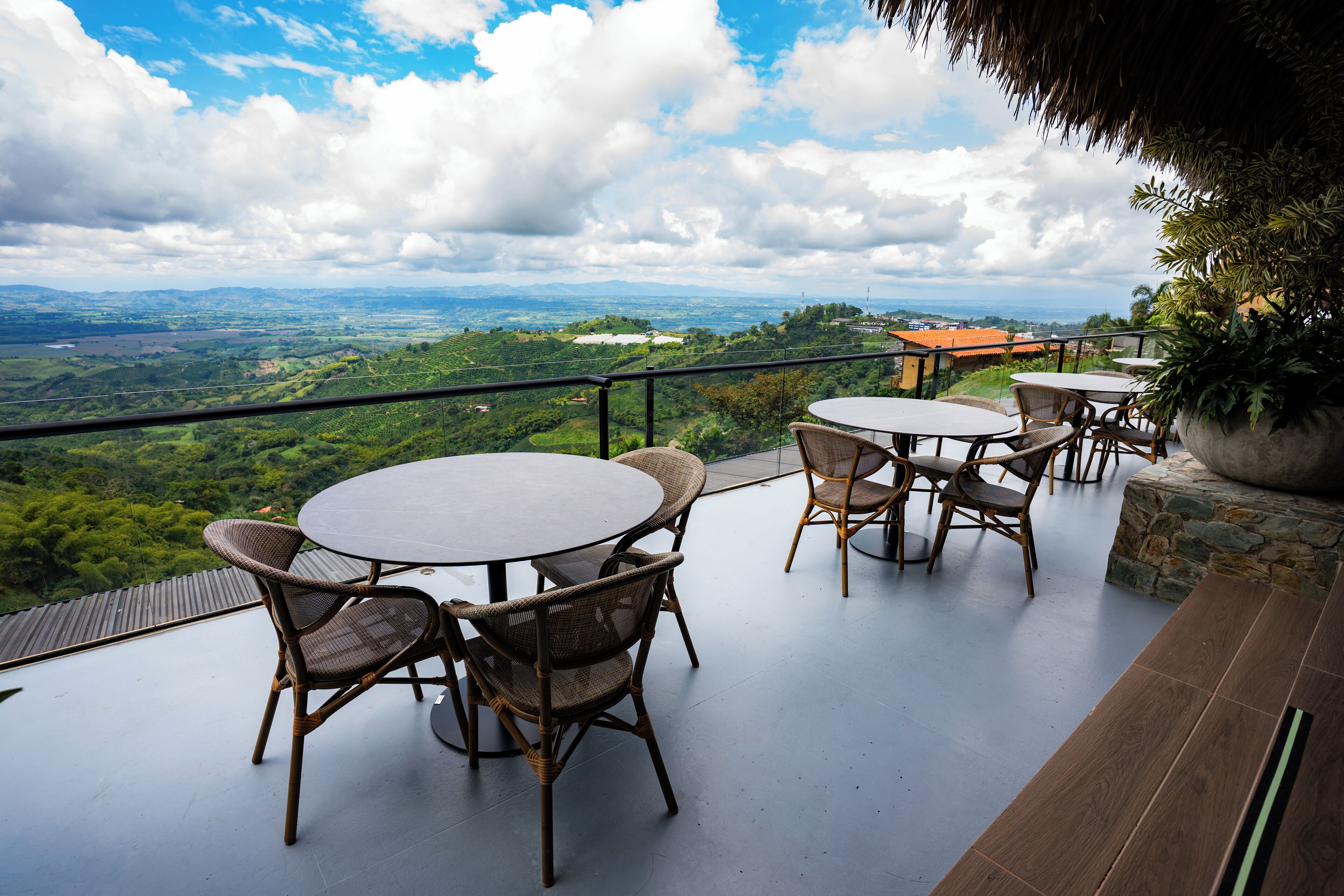 Una terraza con mesas redondas y sillas de mimbre, con vistas a un paisaje pintoresco de colinas y una ciudad distante.
