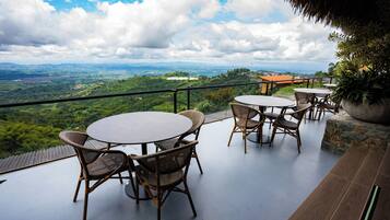 Una terraza con mesas redondas y sillas de mimbre, con vistas a un paisaje pintoresco de colinas y una ciudad distante.